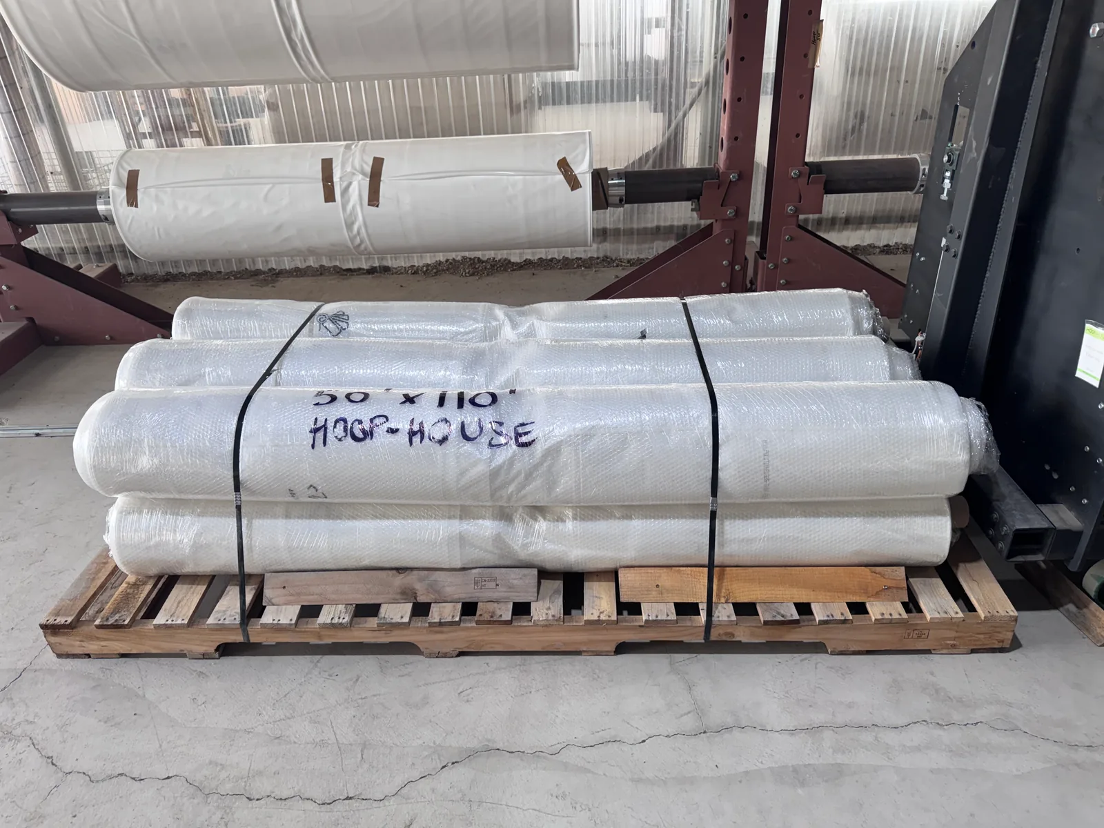 Wrapped hoop-house film rolls marked with their size and strapped to a pallet.