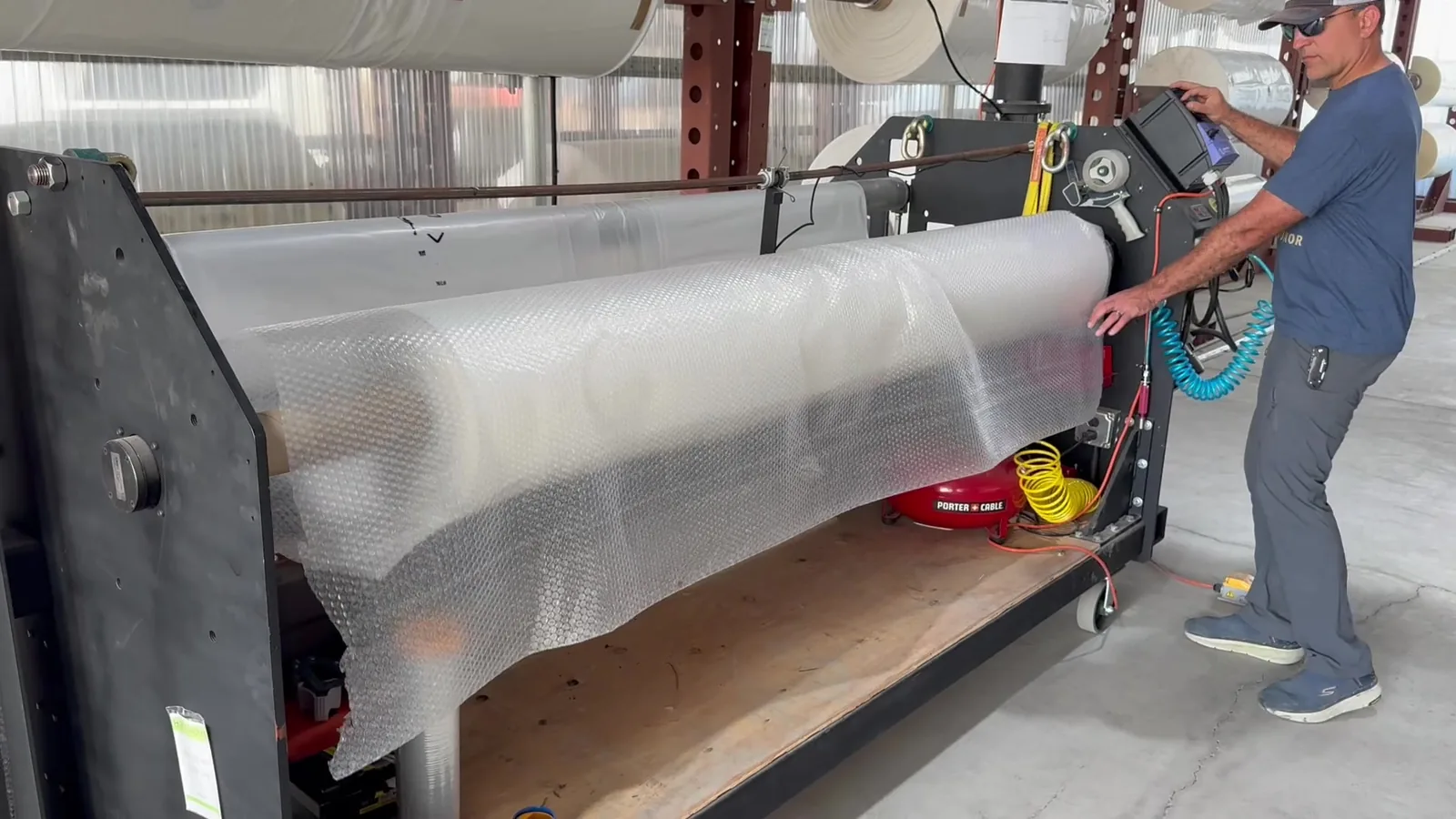 An operator wraps a cut roll of greenhouse film with protective packaging.