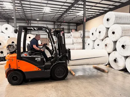 Forklift operator moving a wrapped greenhouse plastic master roll inside the warehouse.